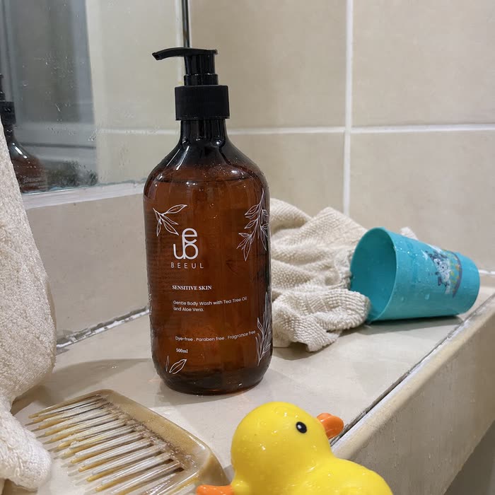 BEEUL Gentle Body Wash on a tiled bath ledge beside a washcloth, a child's bath cup and a rubber duck