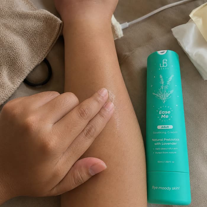 A hand smoothing BEEUL Ease Me Adult cream along a child's forearm on a bed