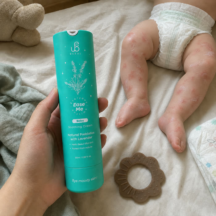 A hand holding BEEUL Ease Me Baby beside a baby lying on a bed with eczema visible on the legs